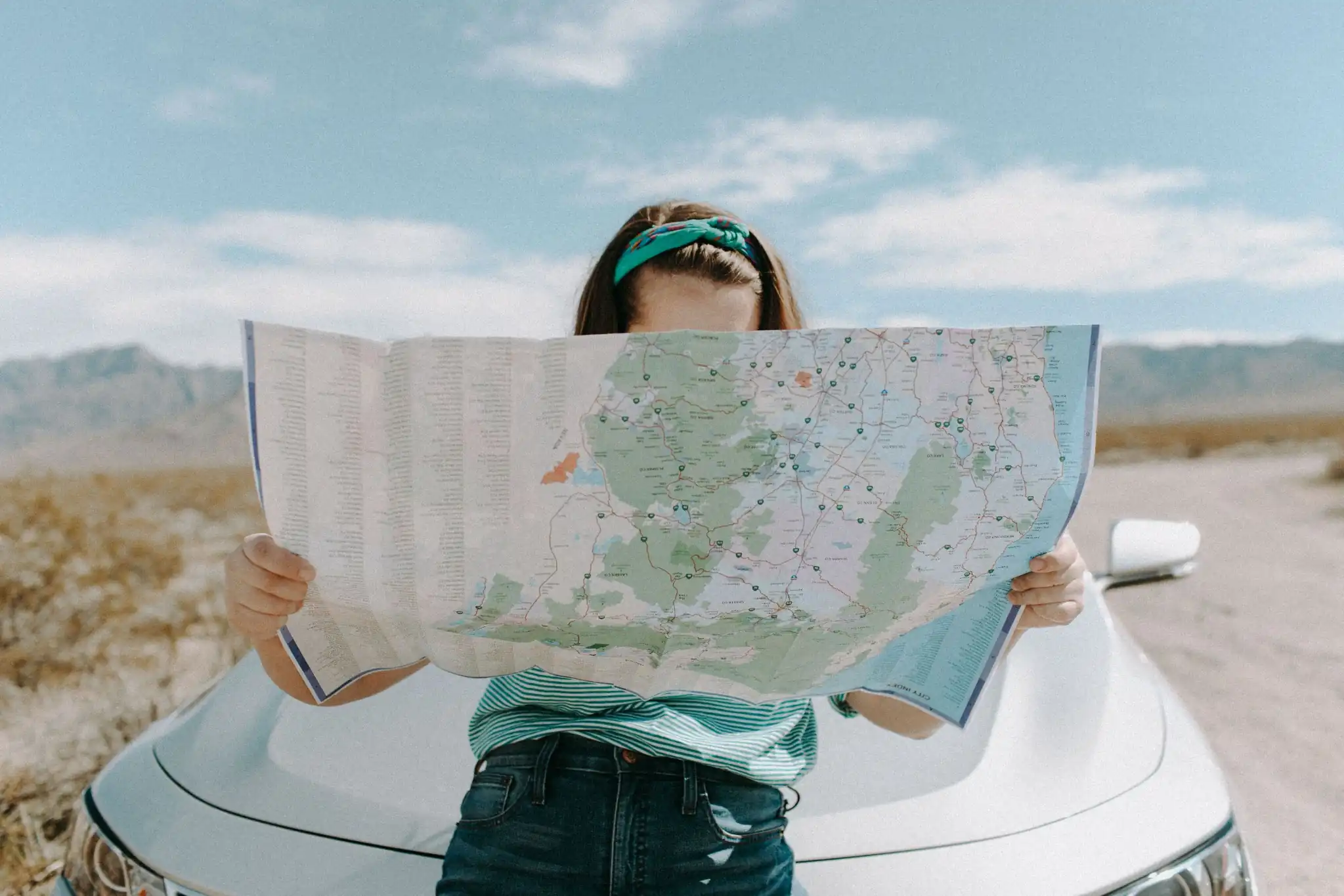 Traveler holding a map while planning a road trip beside a car.